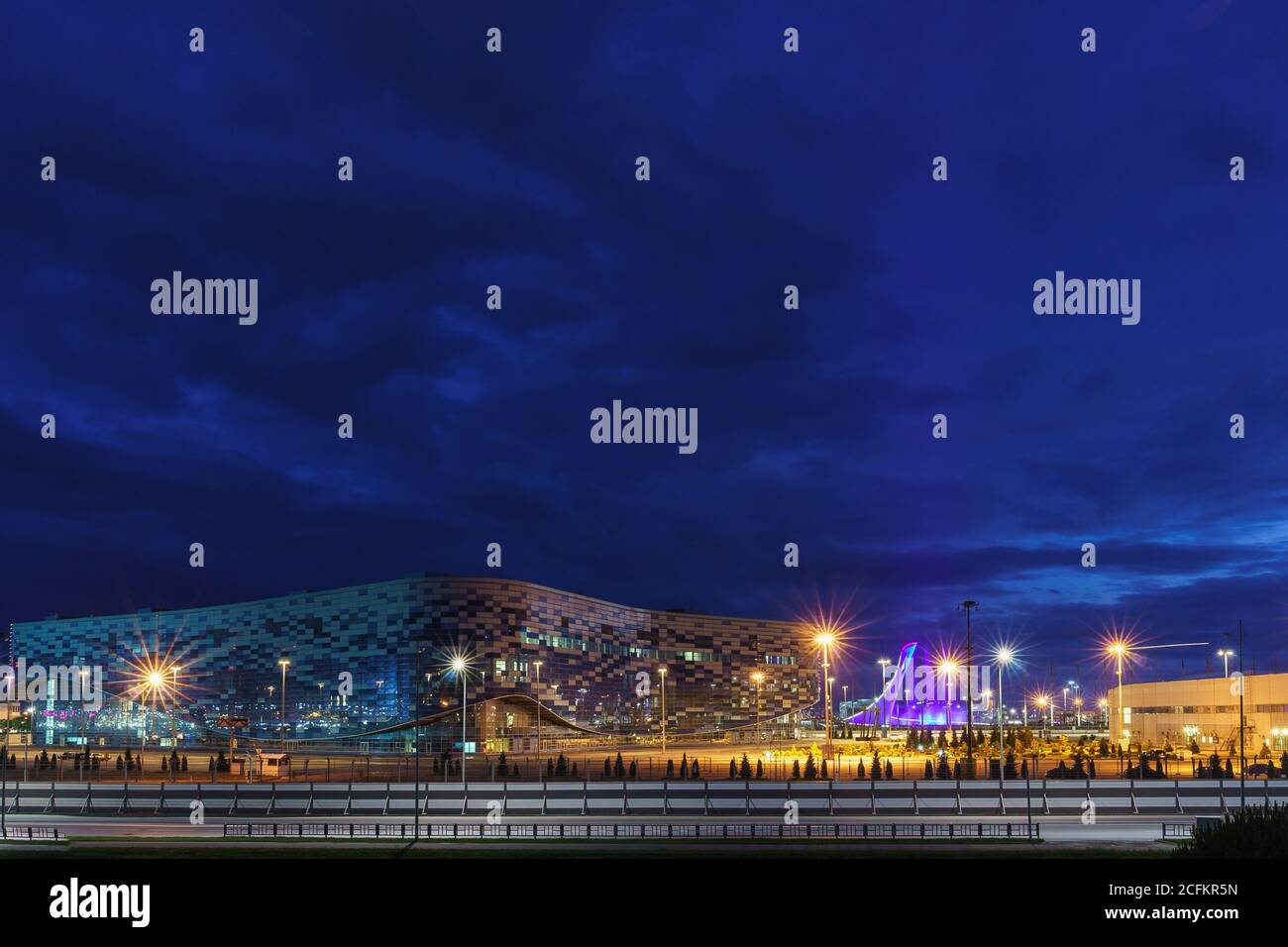 Sotschi, Russland - 11.2017. Juni: Nachtbeleuchtung des Olympiaparks Sotschi: Eissportschalast "Eisberg" und der Licht- und Musikbrunnen unter blauem Himmel Stockfoto