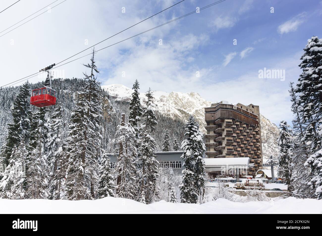 Dombay, Karatschai-Tscherkess Republik, Russland-15. Dezember 2018: Roter Anhänger der alten Seilbahn passiert das verlassene Gebäude des unfertigen Hotels ' Stockfoto