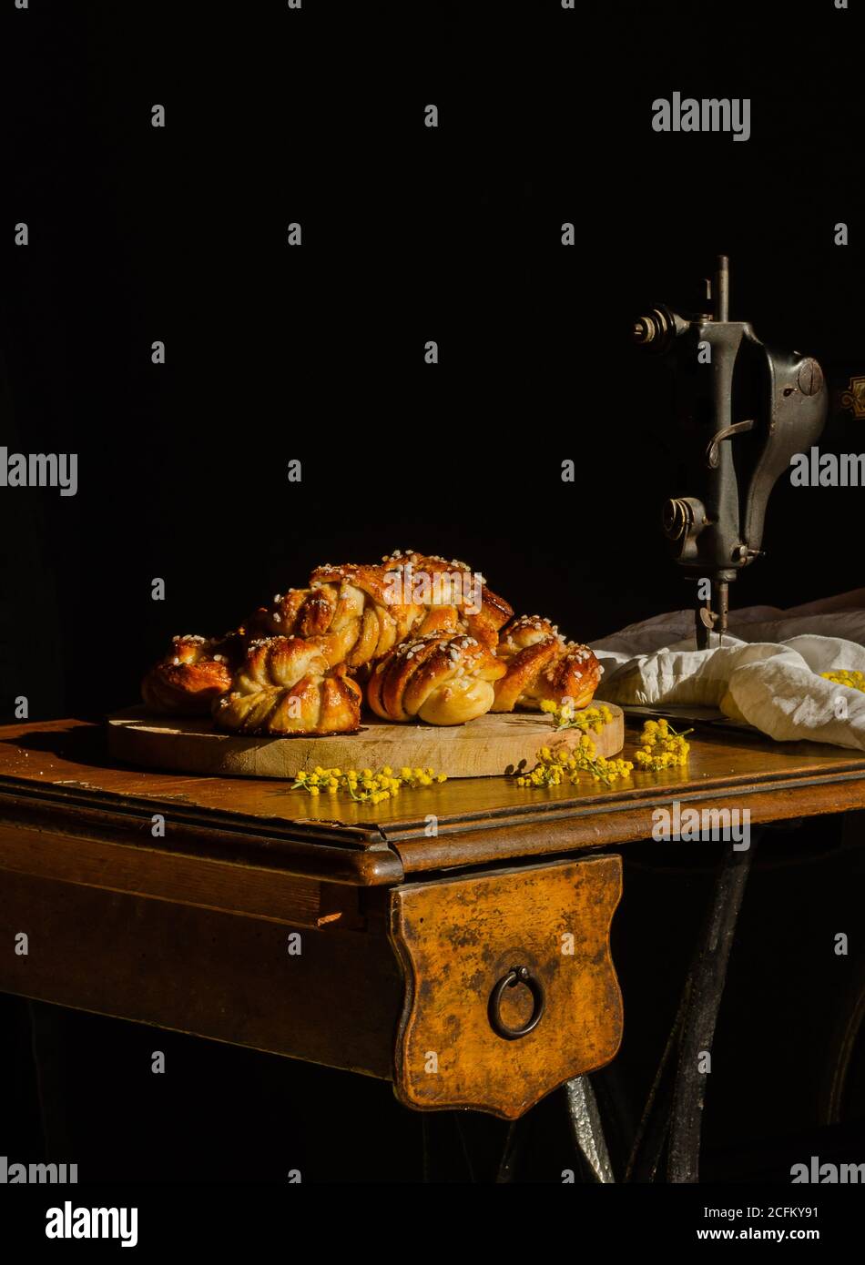 Stapel köstlicher schwedischer Kardamombrötchen auf Schneidebrett gelegt Auf rustikalem Tisch mit Nähmaschine Stockfoto