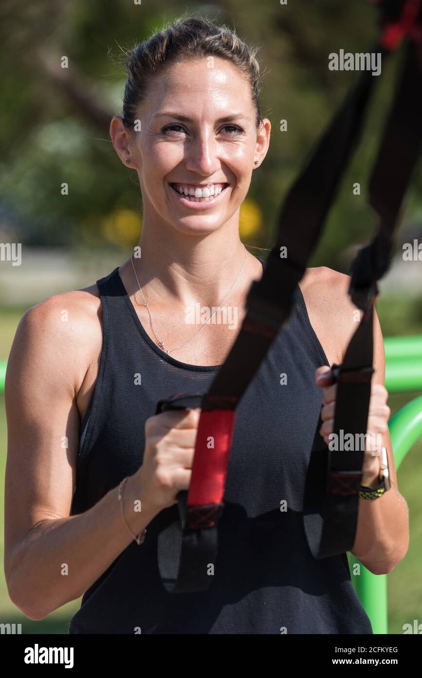 Lächelnde Sportlerin beim Kniebeugen mit TRX-Trägern während des Trainings Im Sommer Stockfoto