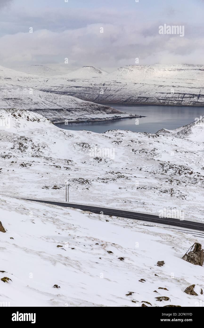 Spektakuläre Landschaft des Flusses umgeben von Bergkette mit bedeckt Schnee im Winter an bewölktem Tag auf den Färöer Inseln Stockfoto