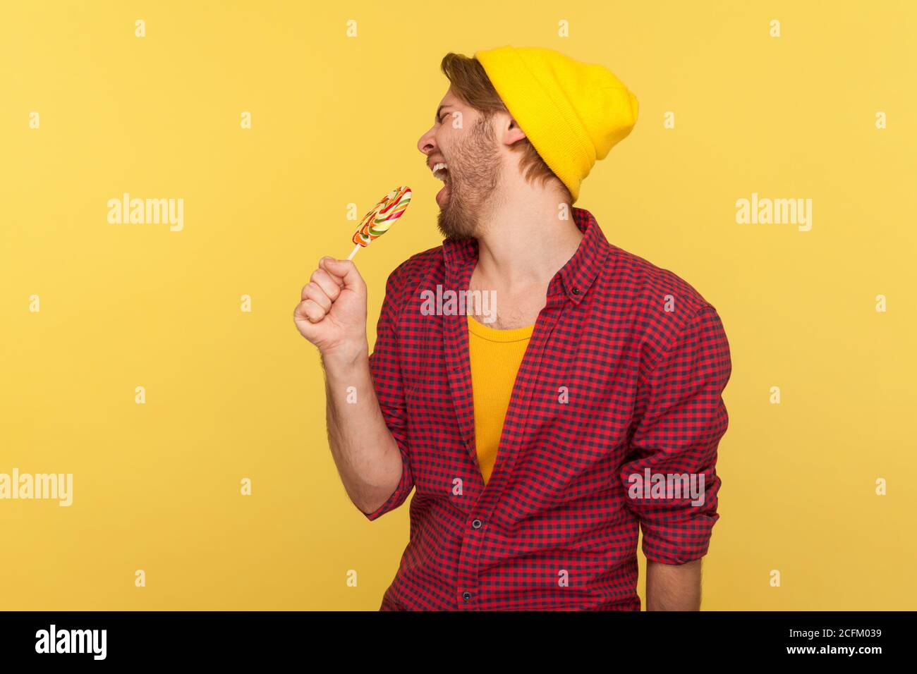 Erstaunlich sorglos Hipster Kerl in Beanie Hut, karierte Hemd schreien in Lollipop wie Mikrofon, singen laut als Popstar in Karaoke, Spaß haben. Stockfoto
