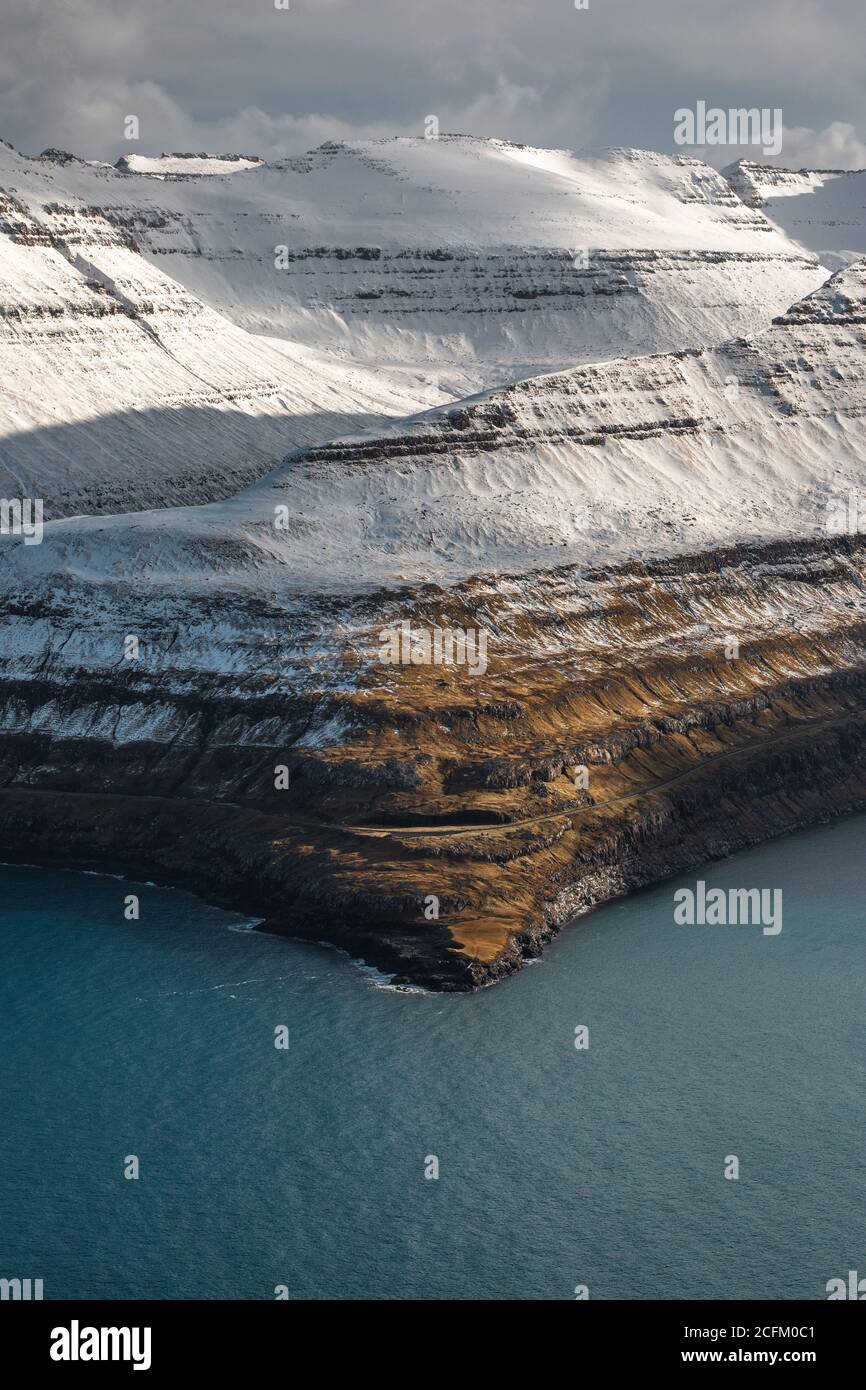 Majestätische Landschaft von felsigen Gelände mit Schnee in der Nähe Ruhe bedeckt Meer an bewölktem Tag auf den Färöern Stockfoto