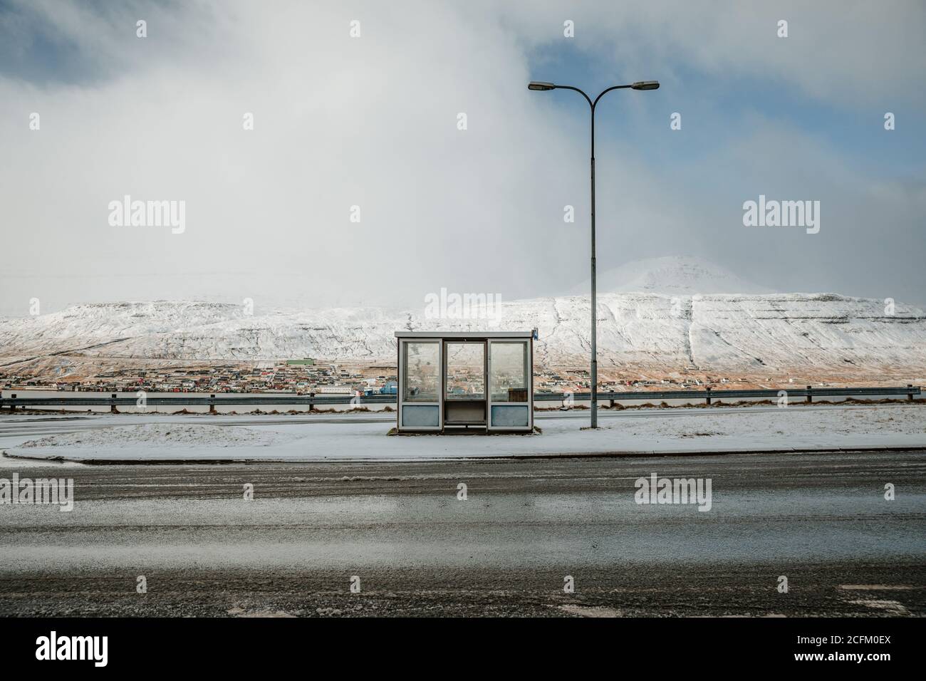 Leere Asphaltstraße mit Schnee bedeckt und von Bergen umgeben An bewölktem Tag auf den Färöern Stockfoto