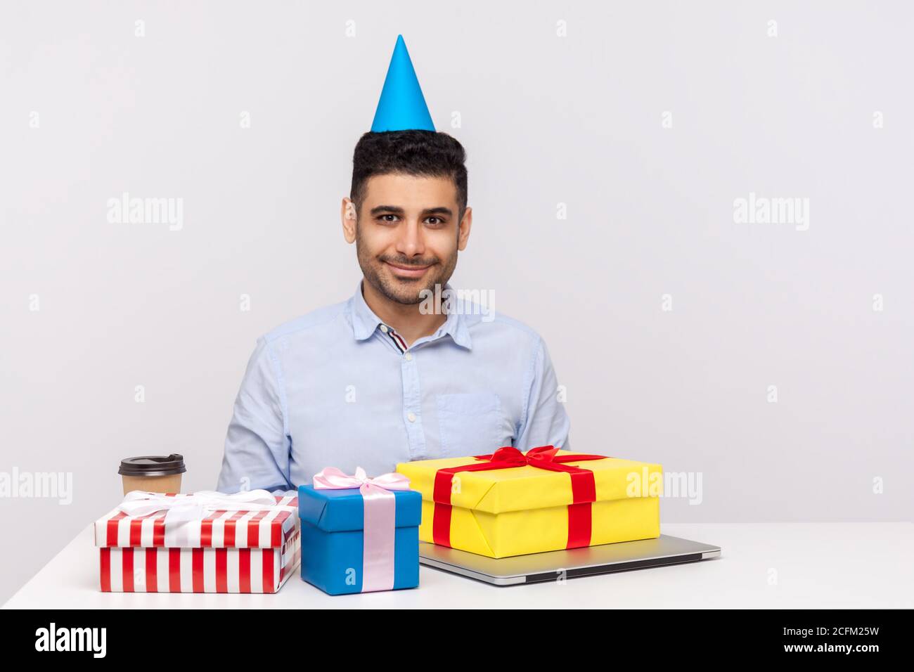 Mann Büroangestellte mit Party-Kegel sitzenden Arbeitsplatz von  Geschenkboxen umgeben und lächelnd freundlich, Geburtstag feiern, genießen  viele Geschenke. ind Stockfotografie - Alamy