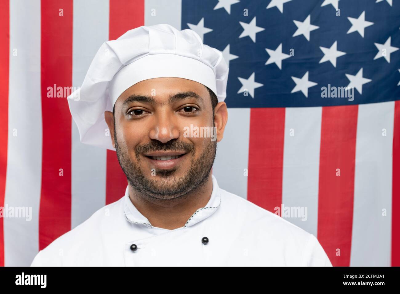 Junger lächelnder Koch des Restaurants in weißer Uniform steht innen Vorderseite der Kamera Stockfoto
