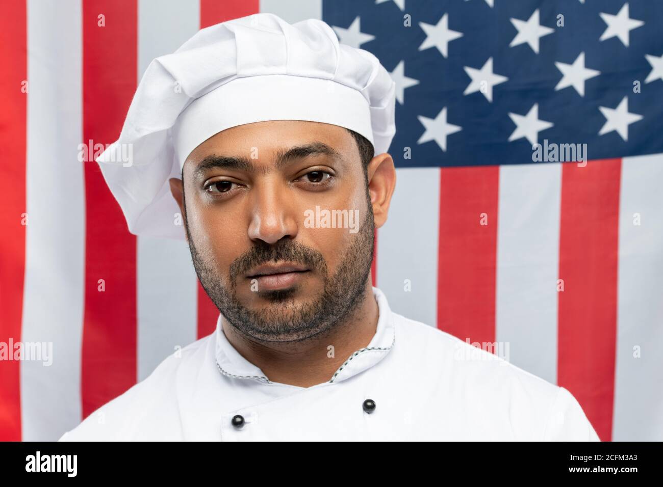 Junge selbstbewusste Mixed-Race-Chef des Restaurants in weißen Uniform suchen Bei Ihnen Stockfoto