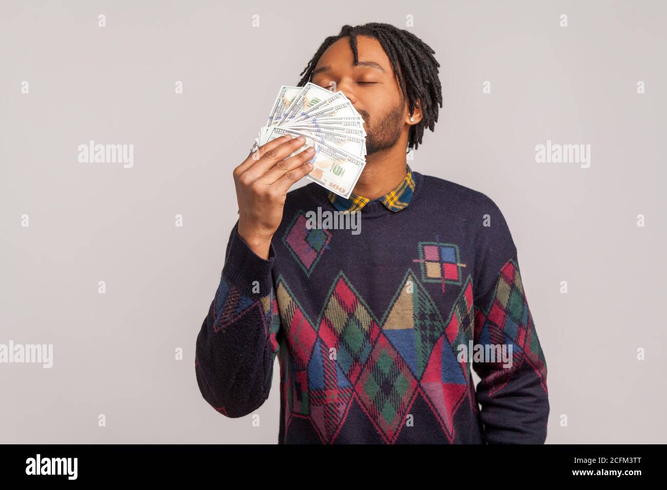 Glücklich zufrieden afrikanischen Kerl mit Dreadlocks und Bart schnüffeln große Partie Geld genießen große Gehalt. Innenaufnahme im Studio isoliert auf grauem Hintergrund Stockfoto