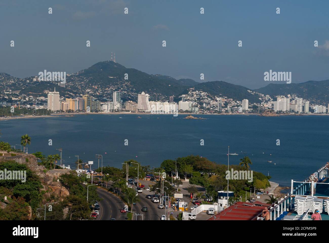 Acapulco, Mexiko - 25. November 2008: Die blaue Wasserbucht mit Strand- und Hochhäusern entlang der Küste. Hintergrund von grünen Hügeln mit Häusern beladen Stockfoto