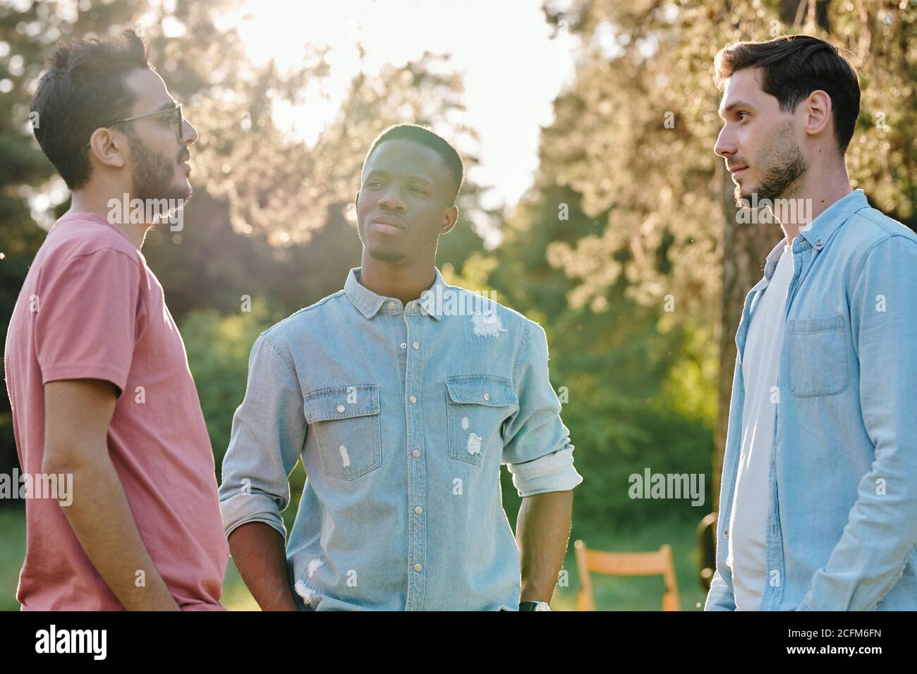 Drei junge interkulturelle Männer in Casualwear, die sich gegenseitig anschauen Während des Chats Stockfoto