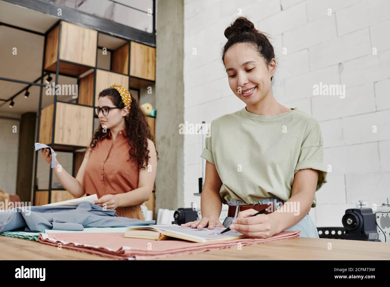 Glückliche junge Modedesignerin zeigt auf Skizze für neue Saison Sammlung Stockfoto