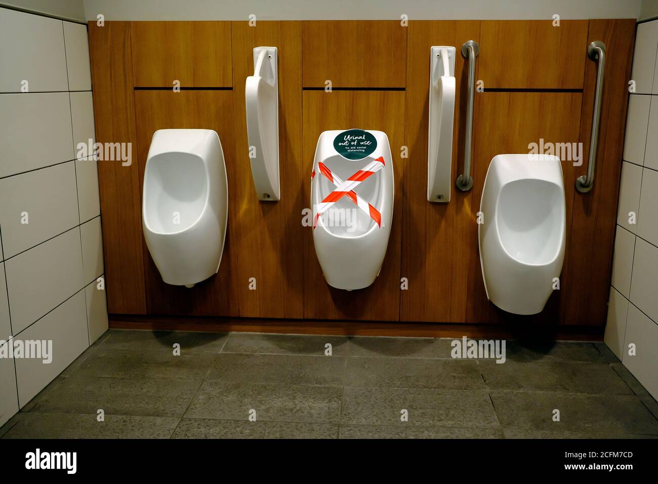 Soziale Distanzierungsmaßnahmen in einer Gentelman-Toilette. Eines der Urinale wird verwendet. Stockfoto