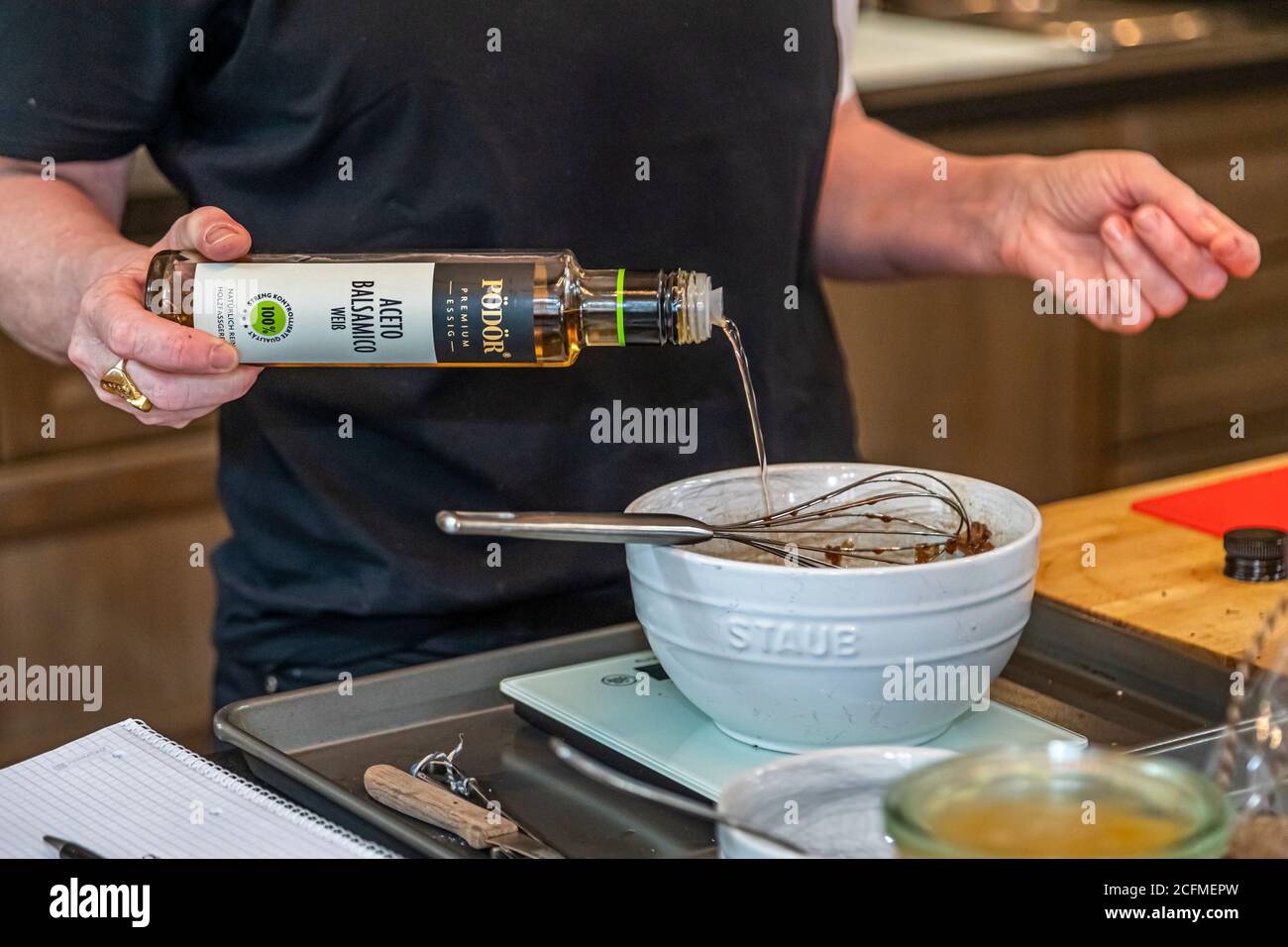 Su Vössing gießt weißen Balsamico-Essig aus der PÖDÖR Ölmühle in eine Schüssel mit Trüffel-Vinaigrette, die auf einer Küchenwaage steht, in ihrer Küche in Stolberg, Deutschland. Präzise Gewichtsangaben statt ungenauer Einheiten sind typisch für ihre Rezepte im neuen Kochbuch. Stockfoto