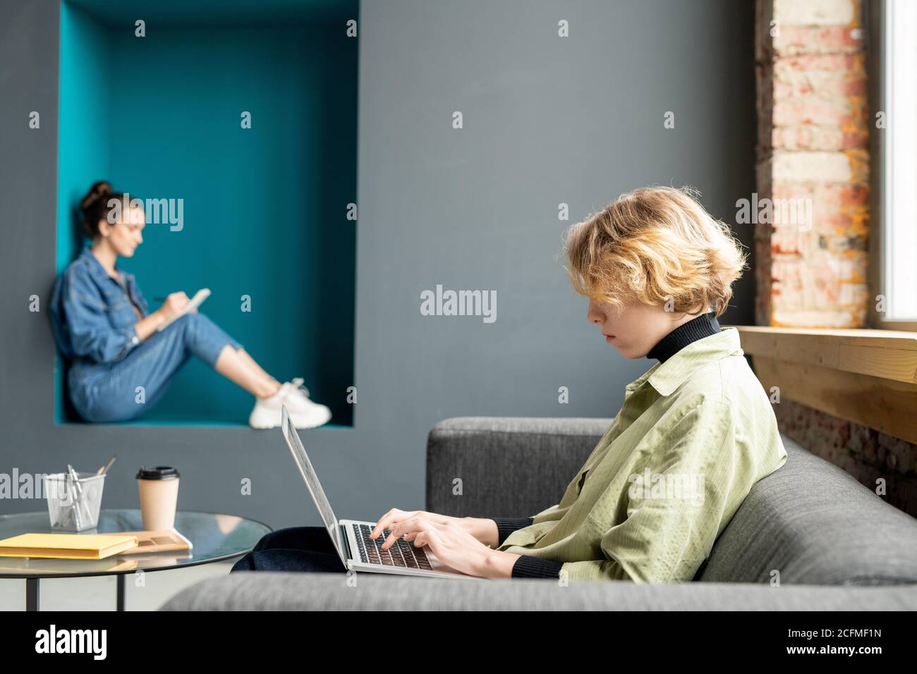 Seitenansicht der jungen blonden weiblichen Büromanagerin in Casualwear Vernetzung auf dem Tisch Stockfoto