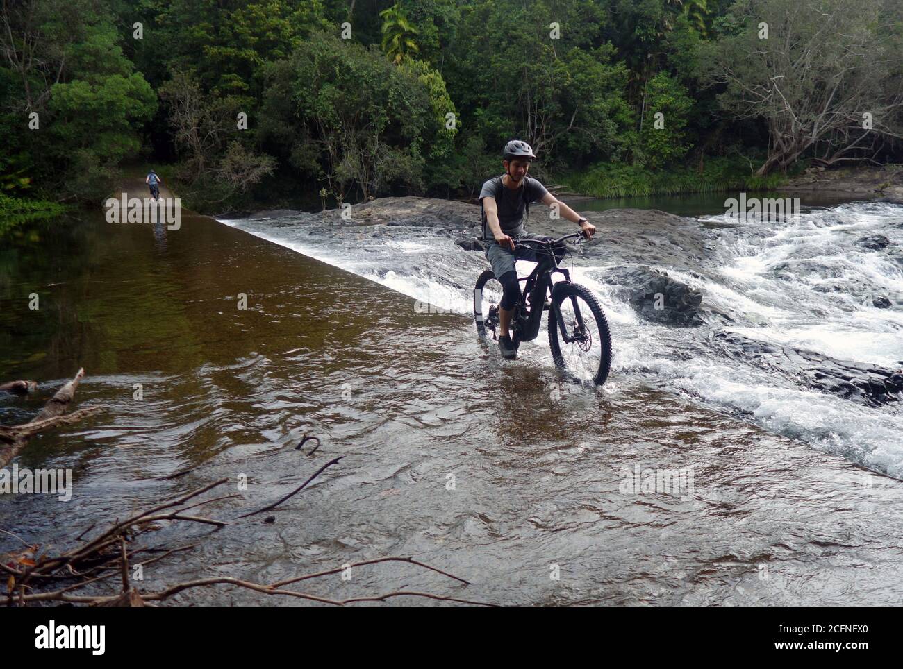 Mann fährt mit dem Elektrofahrrad über den Damm am Little Mulgrave River, Goldfield Trail, Goldsborough Valley, nahe Cairns, Queensland, Australien. Nein, MR Stockfoto