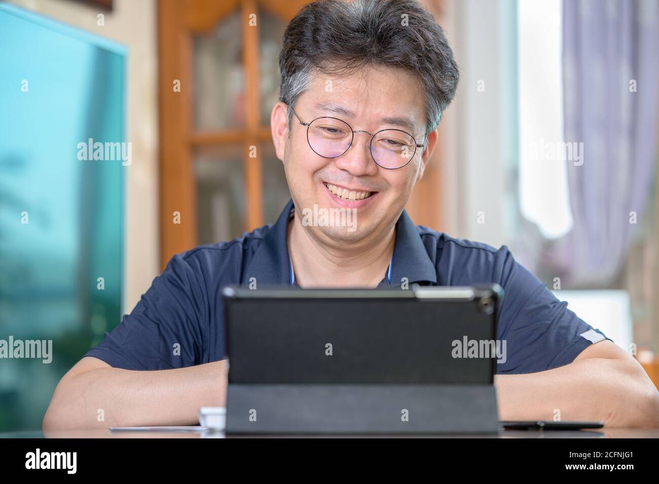 Asiatischer Mann mittleren Alters, der zu Hause arbeitet. Telearbeitkonzept. Stockfoto