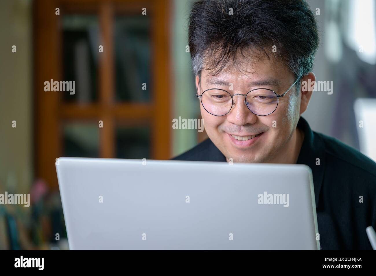 Asiatischer Mann mittleren Alters, der zu Hause arbeitet. Telearbeitkonzept. Stockfoto