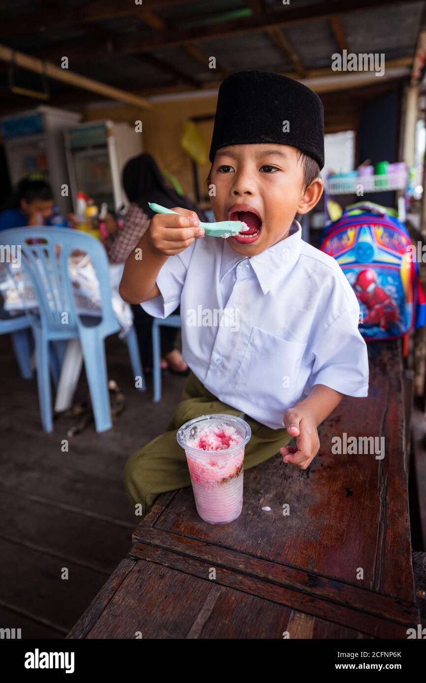 Bandar Seri Begawan / Brunei - 16. Januar 2019: Kleiner muslimischer Junge in Schuluniform mit schwarzem muslimischen Hut beim Essen von gefrorenem Dessert Stockfoto