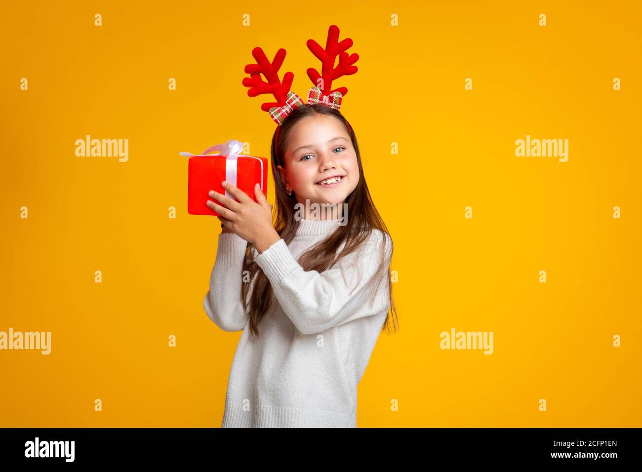 Weihnachten, Ferien und Kindheit. Glückliches Mädchen mit Hörnern hört Geschenk Stockfoto