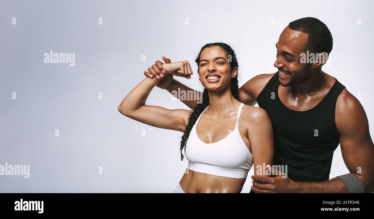 Fröhliche Fitness-Frau, die Spaß hat, Bizeps zu zeigen, wie sie mit männlichen Athleten steht. Fitnesspaare teilen sich nach dem Workout glückliche Momente. Stockfoto