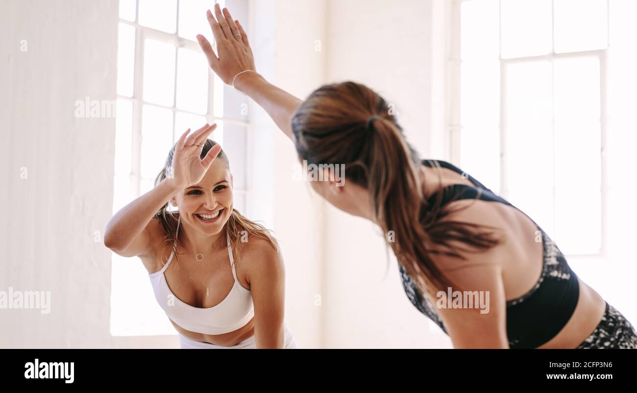 Lächelnde Fitness-Frauen heben die Hände, um eine hohe fünf während des Trainings zu geben. Fröhliche sportliche Frauen genießen das Fitnesstraining in einem Fitnessstudio. Stockfoto