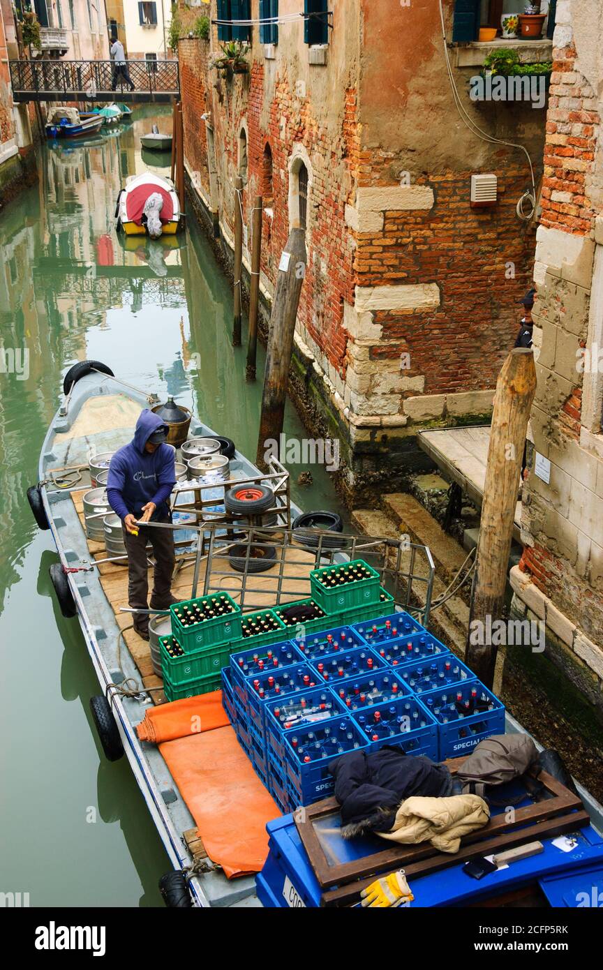 VENEDIG, ITALIEN - 14. FEBRUAR 2015: Ein Mann, der Getränke an die lokalen Pubs und Restaurants verteilt, entlädt Bierkegs und Flaschen von seinem Boot und Uplo Stockfoto