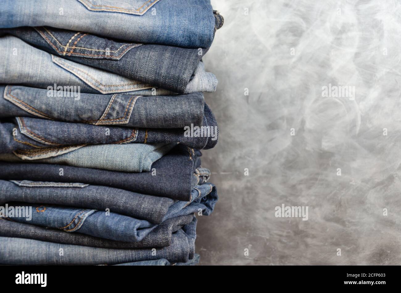 Ein Stapel achtlos gefalteter Jeans auf grauem Hintergrund. Nahaufnahme von Jeans in verschiedenen Farben. Jeans-Struktur oder Denim-Hintergrund. Speicherplatz kopieren Stockfoto