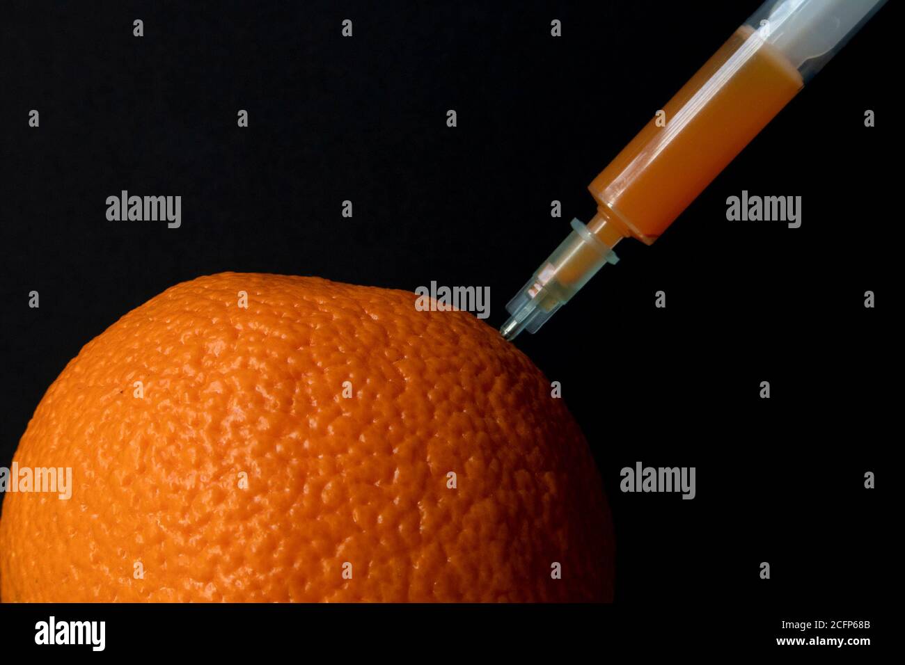 Leuchtendes Orange auf einem Holzbrett und Spritze darin, die orangefarbene Flüssigkeit extrahiert Stockfoto