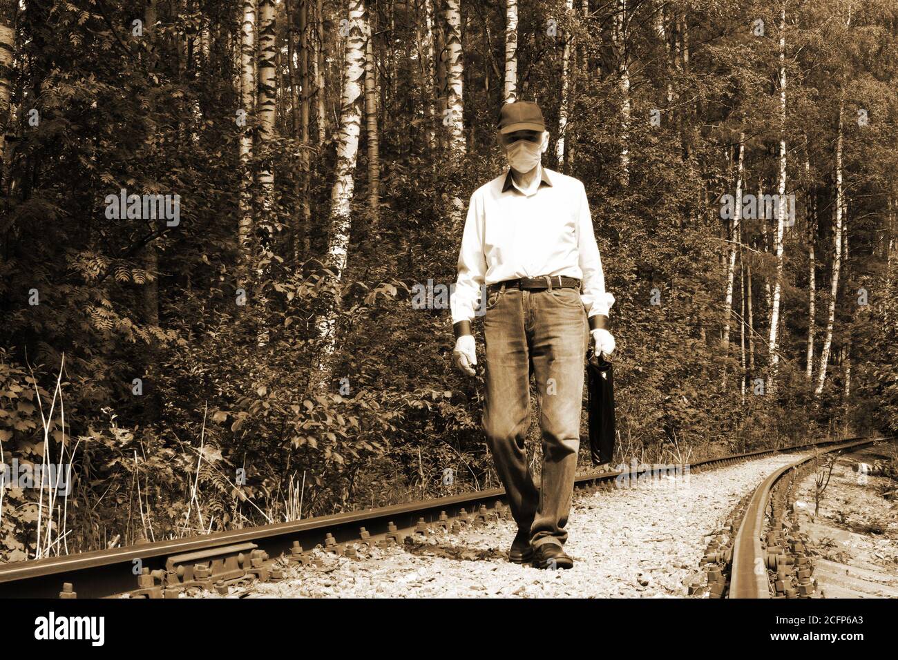 Alter Mann in medizinischer Schutzmaske und Latexhandschuhen, der entlang der alten Eisenbahnstrecke spazierend ist Stockfoto