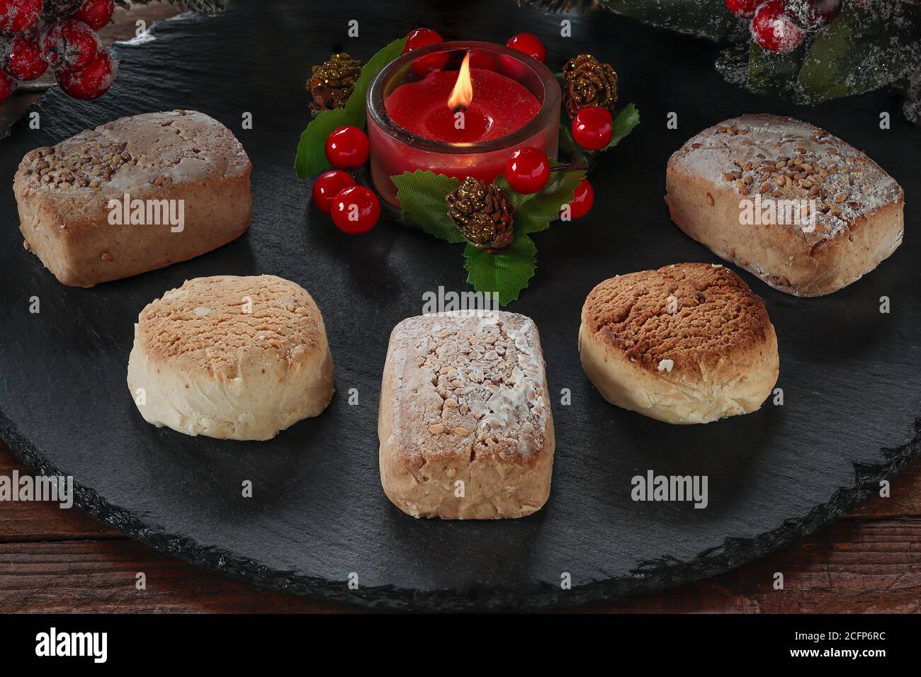 Polvorone und entzündete dekorative rote Kerze auf runder Schieferplatte.Polvoron Ist ein typisches Produkt von Weihnachtsgebäck in Spanien Stockfoto