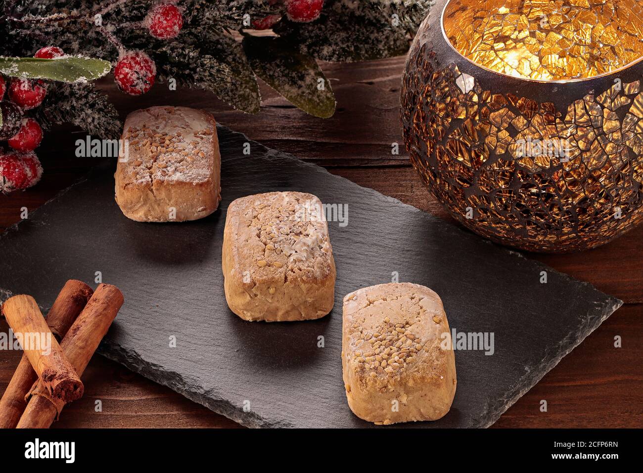 Polvorone auf Schieferteller mit Zimt und Kerzenhalter auf Holztisch. Polvoron ist ein typisches Produkt von Weihnachtsgebäck in Spanien Stockfoto