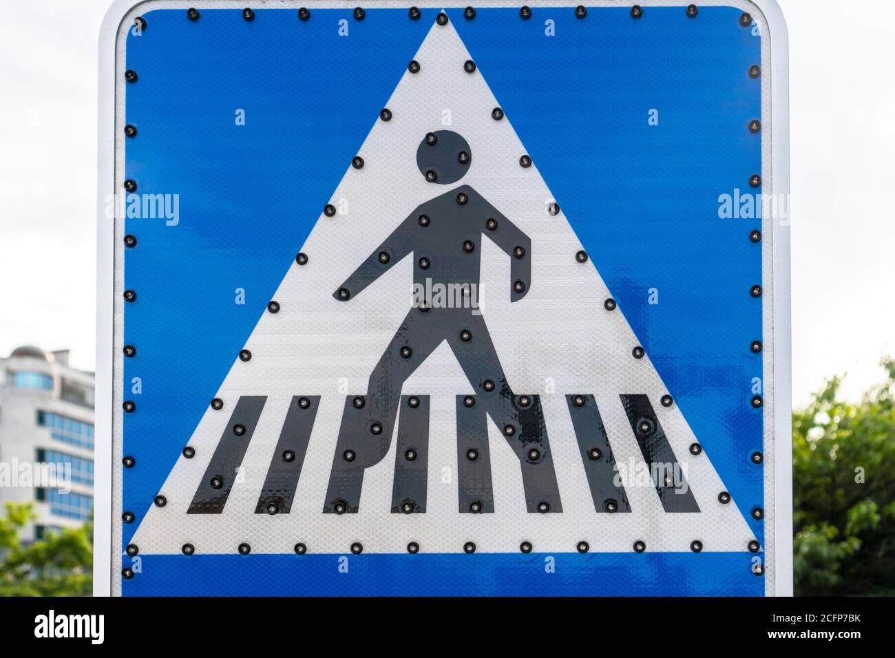 Fußgängerübergangsstraßenschild mit aus LED-Hintergrundbeleuchtung Nahaufnahme vor dem Hintergrund des Himmels, der Stadt und der Bäume. Stockfoto