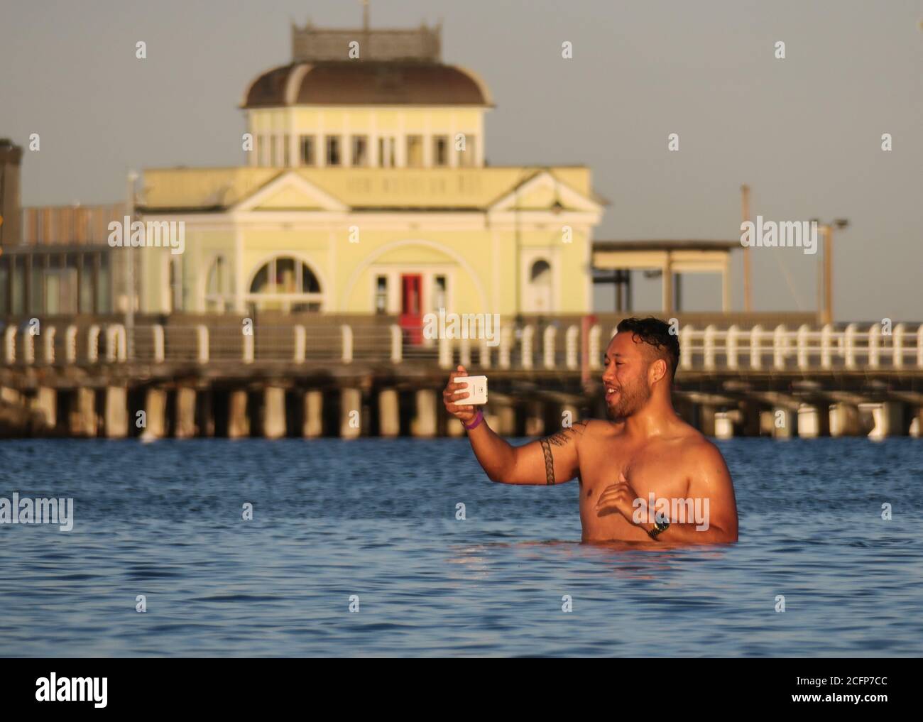 Melbourne Australien; Telefonieren im Wasser bis zur Hüfte. Ein Mann benutzt sein Telefon, während er in Port Phillip Bay ist. Stockfoto