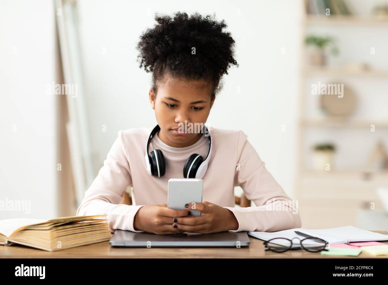 Schwarz Teen Mädchen Mit Telefon Sitzen Bei Laptop Zu Hause Stockfoto