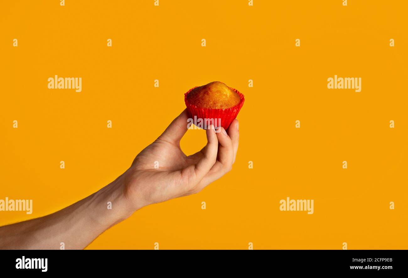 Millennial Kerl hält lecker frischen Muffin über orange Hintergrund, Nahaufnahme Stockfoto