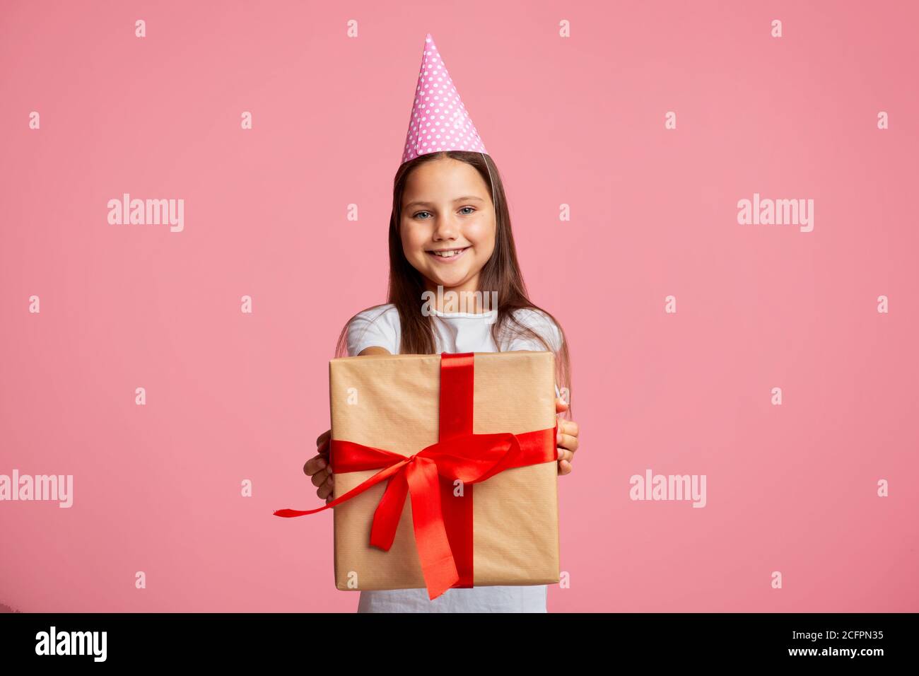 Geburtstagsgeschenk. Happy kleines Mädchen in Mütze mit Geschenkbox mit rotem Band Stockfoto