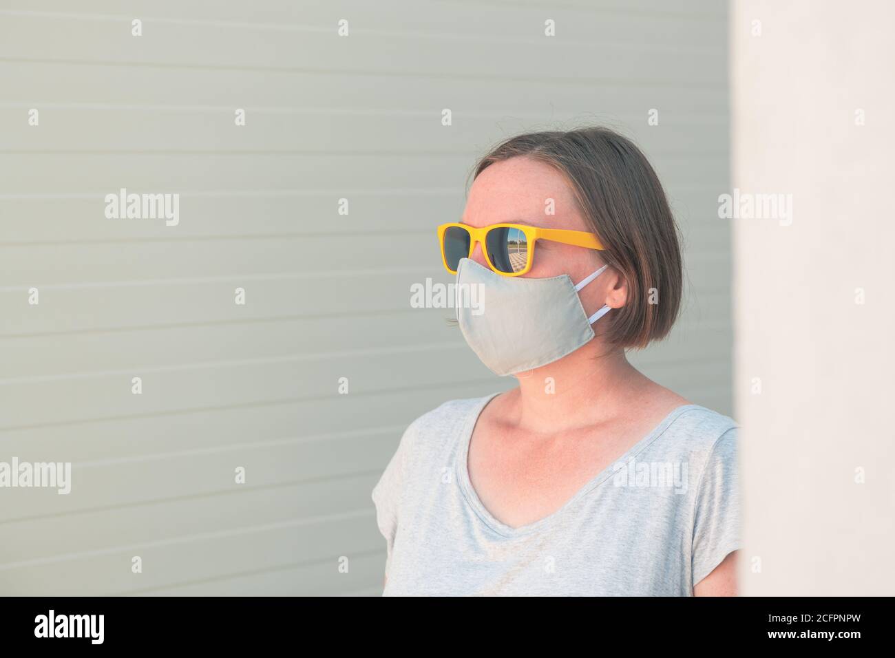 Neue normale, Porträt von casual adult weibliche Person mit Schutzmaske und gelbe Sonnenbrille stehen allein auf der Straße Stockfoto