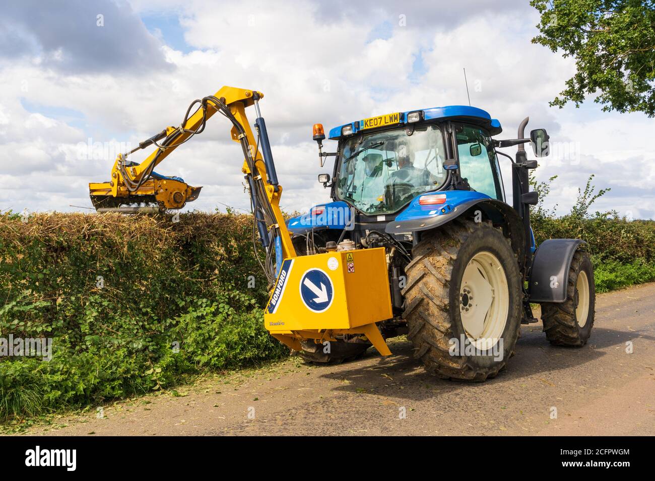 Rückansicht eines Bauern in einem Traktor mit einer Schlegelhecke Hecken in einer Landstraße im Spätsommer geschnitten. Stockfoto