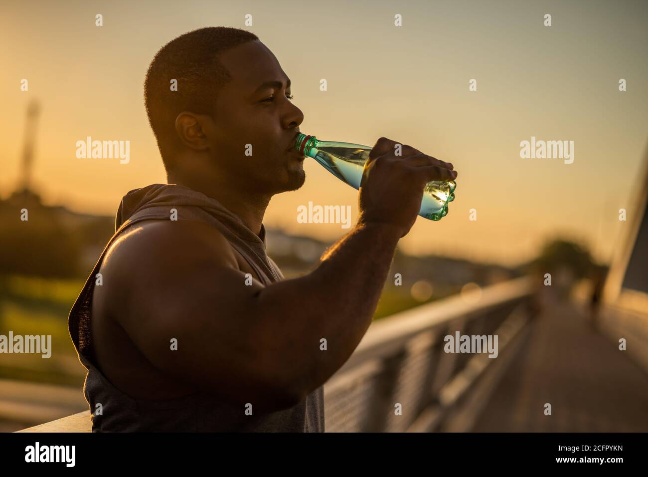 Der junge afroamerikanische Mann trinkt nach dem Training auf der Brücke in der Stadt Wasser. Stockfoto