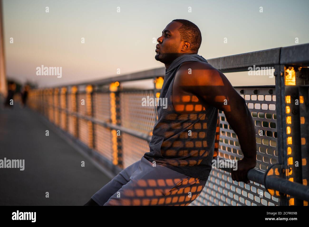 Der junge afroamerikanische Mann trainiert bei Sonnenuntergang auf der Brücke in der Stadt. Stockfoto