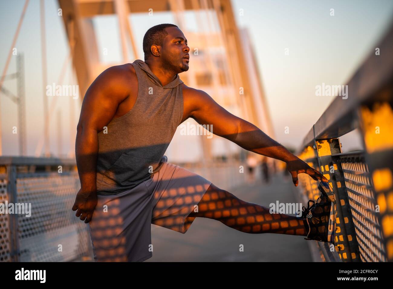 Der junge afroamerikanische Mann trainiert bei Sonnenuntergang auf der Brücke in der Stadt. Stockfoto