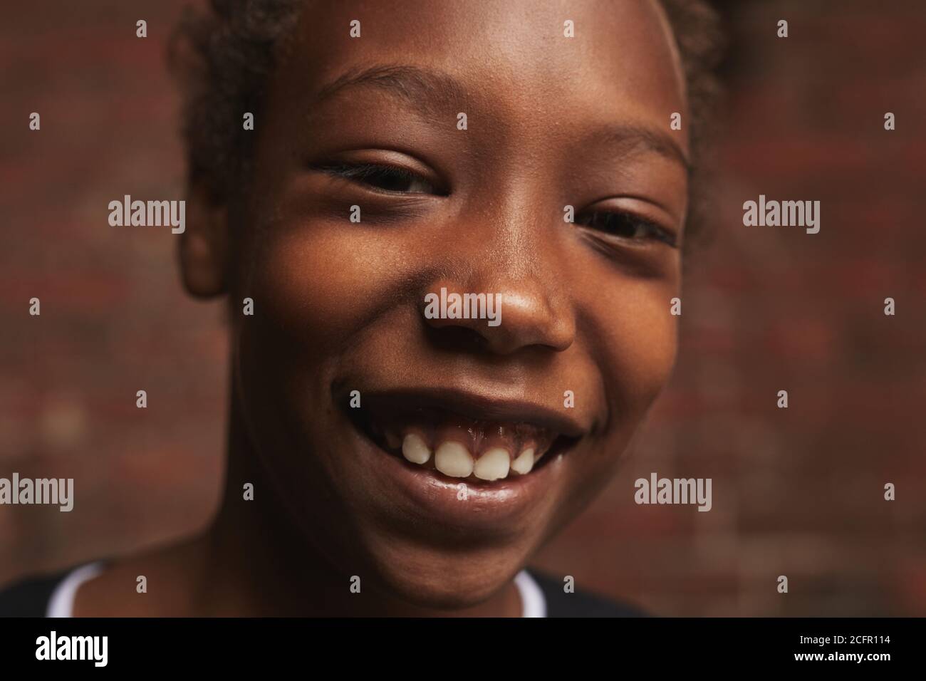 Horizontales Nahaufnahme-Porträt eines hübschen afroamerikanischen Jungen, der gegen eine Mauer steht und die Kamera lächelt und den Raum kopiert Stockfoto