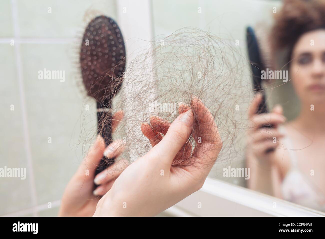Eine Frau zieht ein paar Haare aus ihrem Kamm. Rückansicht. Im Hintergrund eine Spiegelung im Spiegel. Nahaufnahme der Haarbürste. Das Konzept des Haarausfalls. Stockfoto