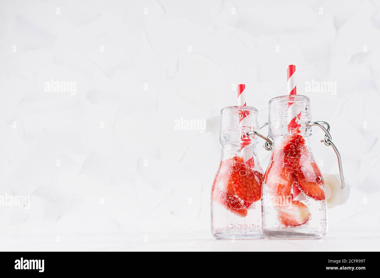 Frische Erdbeer-Limonaden mit geschnittener Beere, Sodawasser, Stroh in durchsichtigen Joch-Flaschen auf weichem hellweißem Holztisch, Kopierraum. Stockfoto