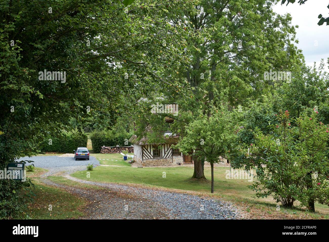 Pfad und Auffahrt flankiert von Bäumen, die zu einem Fachwerk führen Freistehendes normannisches Grundstück mit geparktem Auto Stockfoto