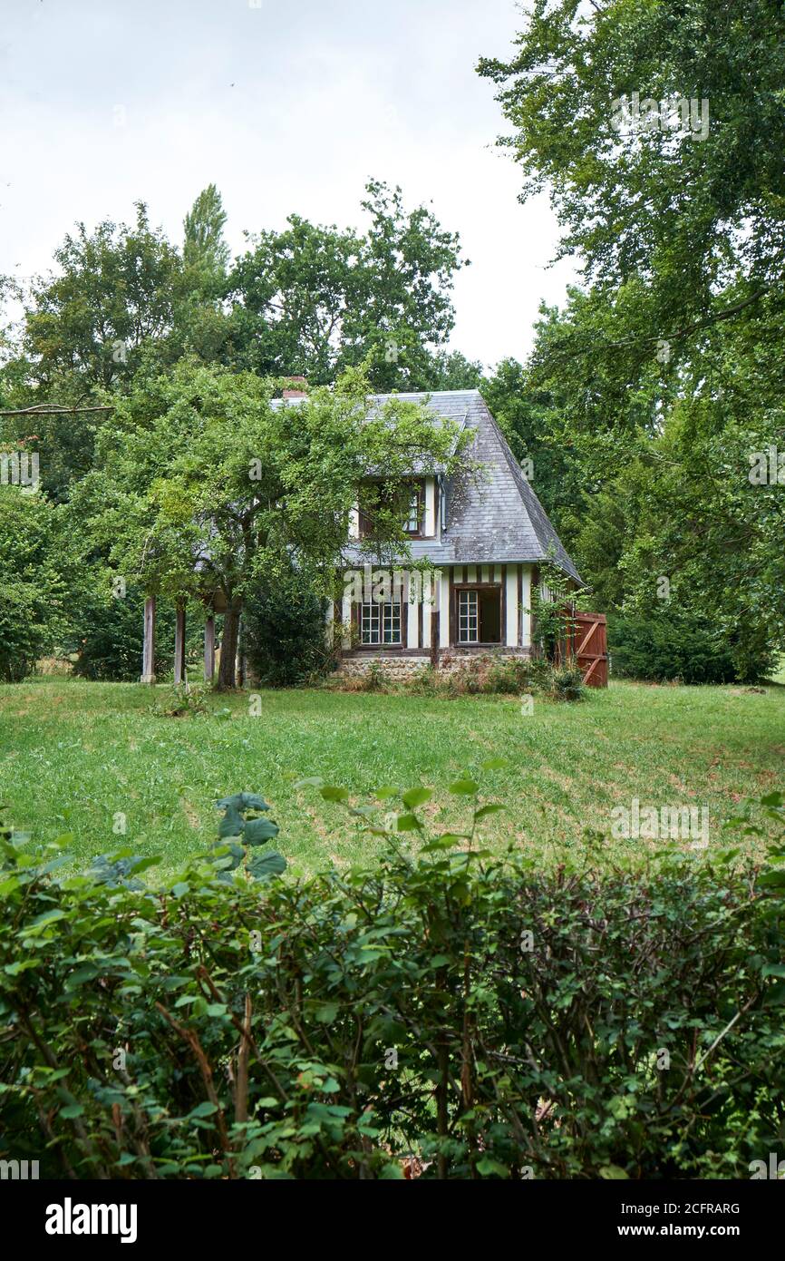 Kleines freistehendes Normannisches Fachwerkhaus mit Schiefer-Ziegeldach umgeben Von Bäumen mit Garten und Hecke im Vordergrund Stockfoto