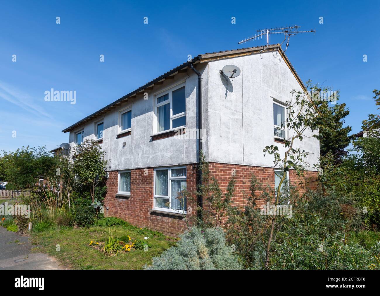 Hinter einem kleinen, modernen 2-stöckigen Wohngebäude/Appartementblock mit ungepflegtem, unordentlichem, chaotischem, überwuchertem Garten in England, Großbritannien. Stockfoto