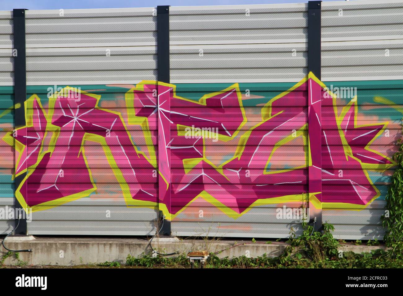 Violette, gelbe und rosa Graffiti an einer Lärmschutzwand Stockfoto