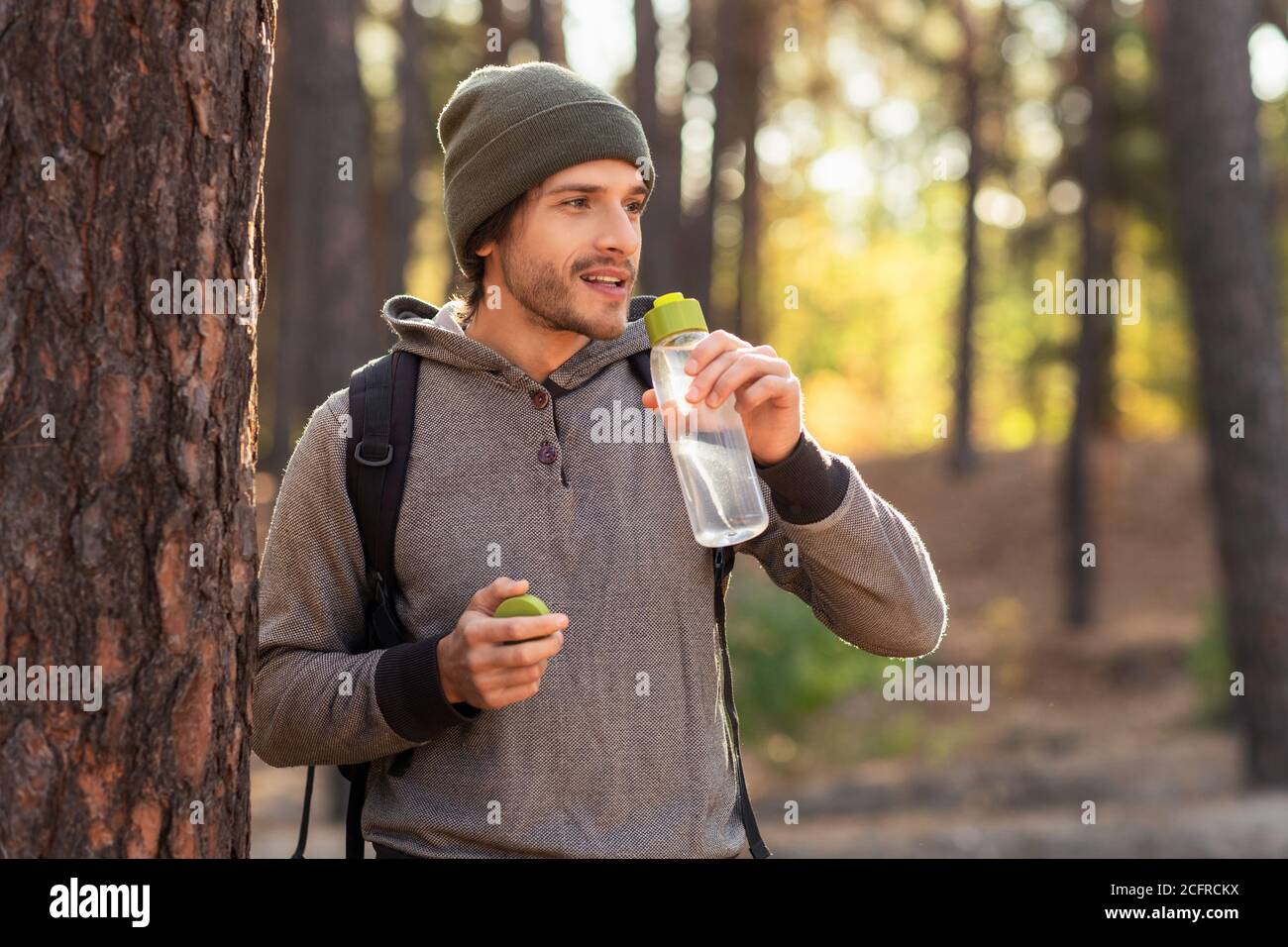 Hübscher Kerl, der Wasser trinkt, während er durch den Wald geht Stockfoto