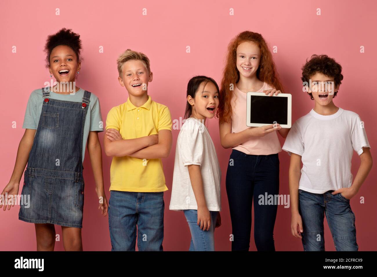 Glücklich diverse Schüler halten Tablet-Computer mit leerem Bildschirm auf rosa Hintergrund, mockup für Design Stockfoto
